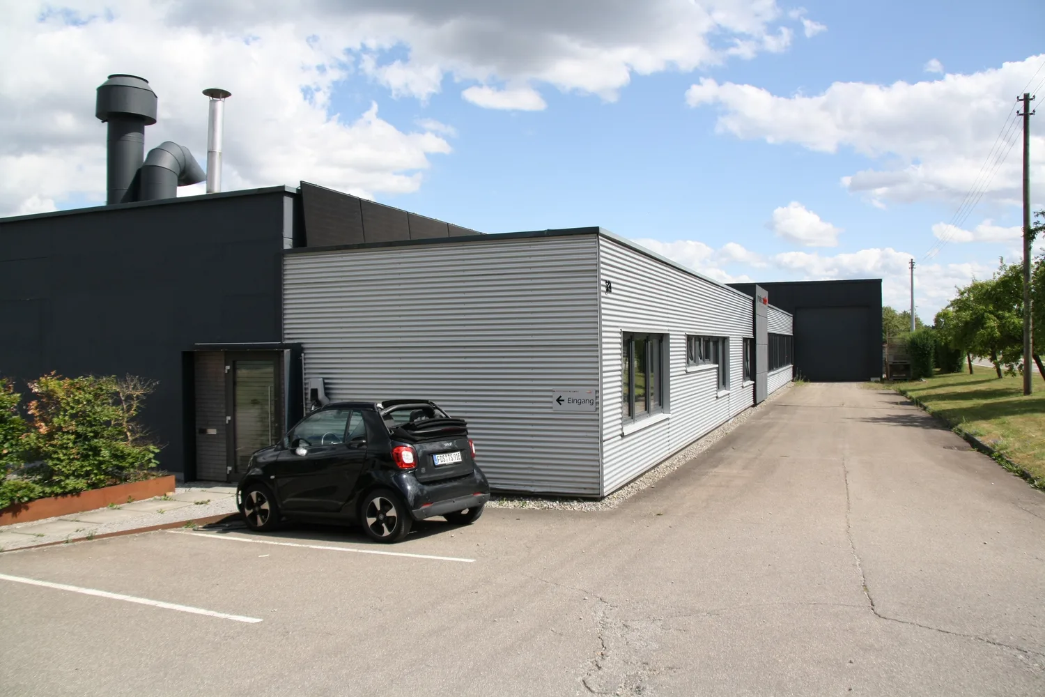 Das Betriebsgebäude von Proteccolor in Pfalzgrafenweiler mit Parkplatz und Zufahrt zur Produktionshalle.