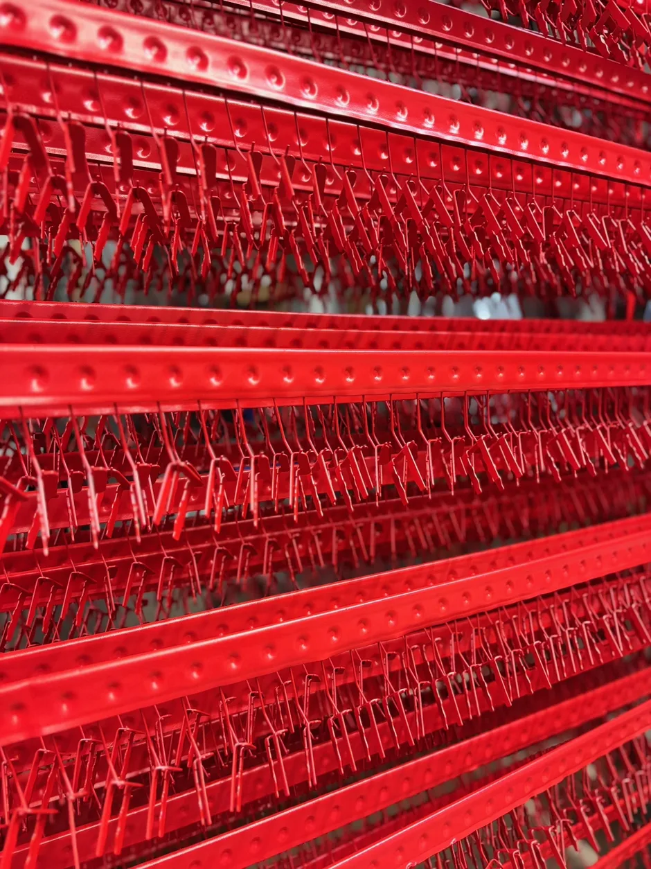 Leuchtend rot pulverbeschichtete Kleinteile hängen dicht an dicht am Gehänge bei Proteccolor.